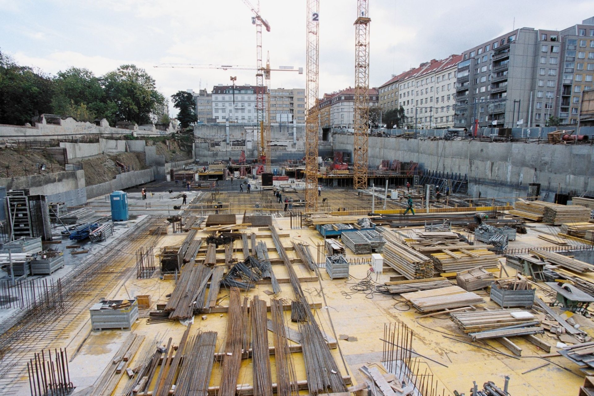 The cut at Flora — the site sloping storeys down to the foundation mat, retaining walls braced against the cemetery property on two sides.